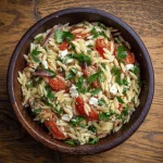 A refreshing cold orzo pasta salad with cherry tomatoes, cucumbers, artichoke hearts, and olives.