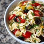 A large bowl of delicious Italian pasta salad with rotini pasta, salami, cherry tomatoes, mozzarella balls, red onion, olives, and fresh parsley.