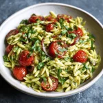 Close-up of a vibrant sun-dried tomato orzo pesto salad with chickpeas, zucchini, feta cheese, and arugula.