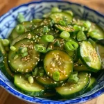 Close-up of a vibrant cucumber salad with green onions and sesame seeds.