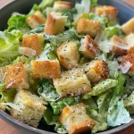 Close-up view of a Caesar salad featuring Romaine lettuce, croutons, and grated Parmesan cheese.