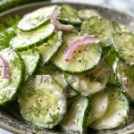 Close-up view of a creamy cucumber dill salad with thinly sliced cucumbers and red onions.