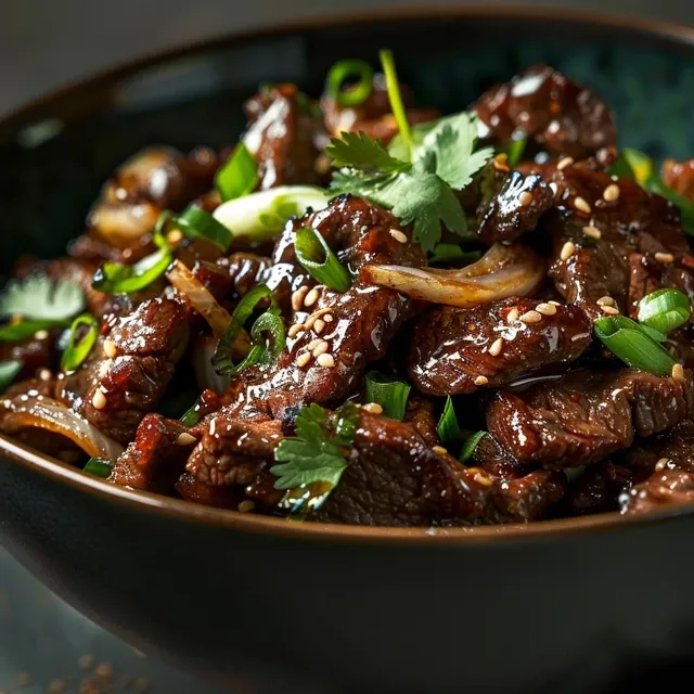 Side view of a bowl filled with stir-fried beef and onions, garnished with green onions and sesame seeds.