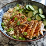 Close-up of sesame noodle bowl with colorful ingredients, including diced cucumbers and edamame.
