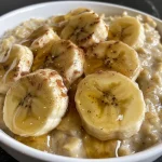 A close-up view of creamy banana oatmeal topped with banana slices and a sprinkle of cinnamon.
