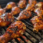 Close-up view of juicy BBQ chicken pieces on a grill.