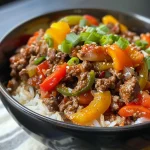 Close-up view of a beef and pepper rice bowl with colorful peppers and minced garlic.
