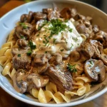Close-up view of a bowl of creamy Beef Stroganoff with noodles and garnished with parsley.