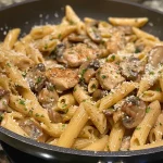 Close-up view of creamy chicken and mushroom pasta in a white bowl, with herbs sprinkled on top.