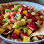 Close-up of colorful fresh fruit salsa in a bowl with crispy cinnamon sugar pita chips beside it.