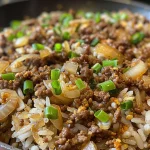 A close-up shot of a ground beef and onion rice skillet with visible grains of rice and chopped green onions.