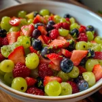 Close-up view of a vibrant fruit salad featuring green grapes, strawberries, and blueberries.