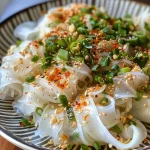 Close-up view of juicy rice paper noodles garnished with herbs and cucumbers.