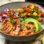 Close-up side view of a shrimp and avocado bowl with colorful mango salsa.