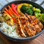 Close-up view of a colorful chicken and veggie power bowl with rice and fresh ingredients.