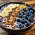 A close-up view of a blueberry oats peanut butter smoothie bowl topped with fresh fruits and chia seeds.