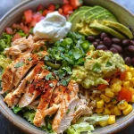 A close-up side view of a colorful Burrito Bowl filled with rice, chicken, and fresh toppings.