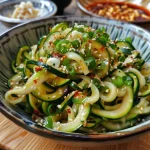 Close-up view of a bowl of zoodles made from zucchini, topped with sesame seeds and green onions.