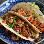 A close-up side view of juicy Mexican ground beef tacos on a plate.
