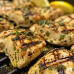 Close-up of grilled lemon herb chicken garnished with herbs.