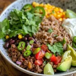 Close-up view of a colorful ground beef burrito bowl, featuring rice, beans, avocado, and fresh vegetables.