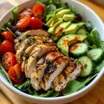 ['Close-up view of a colorful Healthy Chicken Salad Bowl filled with mixed greens, cherry tomatoes, and sliced avocado.', 'Side view of a vibrant chicken salad topped with sunflower seeds and drizzled with a vinaigrette.', 'Juicy chicken breast on a bed of fresh salad ingredients including cucumbers and red bell pepper.', 'Detailed image of a healthy salad bowl featuring protein-rich chicken and various fresh vegetables.']