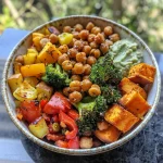 Close-up view of a colorful roasted vegetable and chickpea bowl drizzled with tahini dressing.
