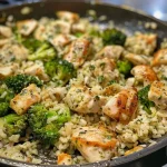 Close-up side view of a skillet filled with cheesy chicken, broccoli, and rice.