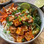 Close-up view of a colorful Spicy Peanut Tofu Bowl with rice noodles and fresh vegetables.