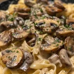 A close-up side view of creamy vegan mushroom pasta garnished with fresh herbs.