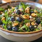 ['A vibrant Blueberry Quinoa Salad with fresh blueberries, feta cheese, and candied walnuts.', 'A close-up view of a colorful Blueberry Quinoa Salad with arugula and sliced red onion.', 'A side view of a Blueberry Quinoa Salad showcasing blueberries, walnuts, and feta on a plate.', 'A detailed shot of a Blueberry Quinoa Salad filled with greens, berries, and nuts, elegantly arranged.']
