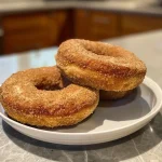 ['Close-up view of healthy apple cider protein donuts with a golden-brown glaze.', 'Side view of moist apple cider donuts topped with a light sprinkle of cinnamon.', 'Delicious-looking protein donuts made with apple cider, showing a soft texture.', 'Juicy apple cider donuts, showcasing their round shape and healthy ingredients.']