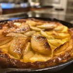 ['Close-up view of a golden-brown Apple Dutch Baby with sliced apples on top.', 'Side view of a fluffy Apple Dutch Baby, with caramelized apple slices and a dusting of cinnamon.', 'Juicy Apple Dutch Baby served in a cast-iron skillet, featuring thin apple slices and a lightly browned crust.', 'Deliciously baked Apple Dutch Baby with a golden crust and tender apple slices, perfect for brunch.']