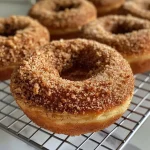 ['Close-up view of golden-brown baked apple cider donuts with a sprinkle of cinnamon sugar.', 'A side view of baked apple cider donuts, showcasing their fluffy texture and rich color.', 'Juicy baked apple cider donuts arranged attractively, highlighted by a dusting of cinnamon.', 'Delicious baked apple cider donuts with a glossy finish and a hint of apple spice.']