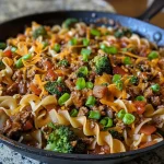 ['A juicy Beef Noodle Skillet filled with ground beef, broccoli, and egg noodles.', 'Close-up view of a Beef Noodle Skillet highlighting diced onions, garlic, and melted cheese.', 'A colorful Beef Noodle Skillet featuring broccoli florets and sliced green onions on top.', 'Side view of a savory Beef Noodle Skillet, showing creamy sauce and vibrant ingredients.']