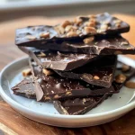 ['Close-up view of chocolate peanut butter cup bark with mini peanut butter cups embedded.', 'Side view of a delectable chocolate and peanut butter layer dessert.', 'Texture-rich chocolate bark featuring peanut butter chips and mini cups.', 'Layered sweets highlighting shiny dark chocolate and peanut butter elements.']