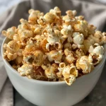 ['Close-up of golden-brown cinnamon popcorn scattered on a surface.', 'Side view of cinnamon-flavored popcorn with a glossy texture.', 'A pile of cinnamon popcorn glistening with melted butter and sugar.', 'Deliciously coated popcorn with a dusting of cinnamon and sugar.']