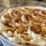 ['Close-up view of creamy cinnamon roll cheesecake dip in a serving bowl.', 'Side view of a luscious cinnamon roll cheesecake dip topped with a sprinkle of cinnamon.', 'Creamy dip with a rich cinnamon swirl, served in a bowl with a spoon.', 'Thick and creamy cheesecake dip with a cinnamon roll flavor, displayed on a wooden table.']