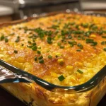 ['Close-up view of a juicy cornbread casserole with a golden crust.', 'Side view of cornbread casserole topped with sliced chives.', 'Juicy cornbread casserole showcasing its fluffy texture and butter drizzle.', 'Delicious cornbread casserole with visible layers of corn and sour cream.']