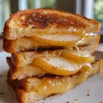 ['Side view of a gooey apple cheddar grilled cheese sandwich on sourdough bread.', 'Close-up of a grilled cheese sandwich with melted cheddar and apple slices, golden crust.', 'Sliced sourdough bread filled with cheese and apple, showing a deliciously melted interior.', 'Juicy apple cheddar grilled cheese, showcasing the texture and colors of the filling.']