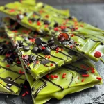 ['Close-up of Frankenstein-themed chocolate bark with green candy melts and eye sprinkles.', 'Side view of colorful Frankenstein chocolate bark featuring green, red, and black icing decorations.', 'Detailed image of Halloween chocolate bark resembling Frankenstein, showcasing vibrant colors and toppings.', 'Tasty Frankenstein chocolate bark displayed with an emphasis on its bright colors and spooky elements.']