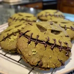 ['Close-up of colorful Frankenstein stitched cookies on a plate.', 'Detailed view of Frankenstein-themed cookies with stitching designs.', "Side angle of freshly baked cookies resembling Frankenstein's face.", 'Handheld photo of unique stitched cookies inspired by Frankenstein.']