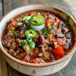 ['Close-up of a bowl filled with chunky, hearty beef chili featuring beans and colorful peppers.', 'Side view of a steaming bowl of ground beef chili, showcasing ingredients like beans, tomatoes, and spices.', 'Juicy beef chili with various beans and peppers, presented in a rustic bowl on a wooden surface.', 'Delicious high-protein chili garnished with cheese and green onions, highlighting its vibrant appearance.']