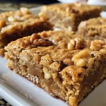 ['Close-up view of maple walnut blondies with a golden-brown crust and visible walnut pieces.', 'Side view of a slice of blondie, showcasing its moist texture and rich, golden color.', 'Delicious blondies featuring chunks of walnuts and a drizzle of maple syrup, captured from a side angle.', 'A slice of maple walnut blondie with a soft, chewy texture and a glossy top, displayed against a simple background.']
