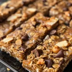 ['Close-up of a peanut butter chocolate chip granola bar with visible chocolate chips and nuts.', 'Side view of a granola bar showing the texture and ingredients like oats and chocolate chips.', 'Juicy granola bar with a glossy sheen of peanut butter and sprinkled chocolate chips.', 'Detailed view of a homemade granola bar featuring chunks of dark chocolate and nuts.']