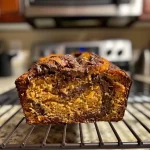 ['A side view of a moist Pumpkin Chocolate Swirl Bread loaf with visible chocolate swirls and pumpkin color.', 'Close-up view of Pumpkin Chocolate Swirl Bread showcasing texture and colors, highlighting its chocolate and pumpkin swirls.', 'A detailed side shot of Pumpkin Chocolate Swirl Bread, emphasizing its rich blend of dark chocolate and golden pumpkin.', 'An appetizing side perspective of Pumpkin Chocolate Swirl Bread, featuring a shiny crust and distinct color contrast.']
