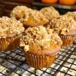 ['Close-up of a pumpkin coffee cake muffin with a rich golden-brown hue, showing the streusel topping.', 'Side view of a warm pumpkin coffee cake muffin, highlighting its moist texture and nutty walnut pieces.', 'Delicious pumpkin coffee cake muffin with a crumbly topping, displayed on a wooden table.', 'A fluffy pumpkin coffee cake muffin cut in half, revealing its moist interior and spices.']