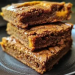 ['Close-up view of a tray of golden-brown pumpkin spice blondies.', 'Side view of moist pumpkin spice blondies with a soft texture.', 'Mouth-watering pumpkin spice blondies displayed on a rustic wooden table.', 'A delicious serving of pumpkin spice blondies with warm spices visible.']
