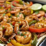 ['Close-up of colorful shrimp fajitas on a sheet pan, garnished with lime wedges and cilantro.', 'Juicy shrimp with sliced bell peppers and onions on a baking sheet ready to serve.', 'Side view of vibrant shrimp fajitas, featuring a mix of bell peppers and flour tortillas.', 'Loaded sheet pan with shrimp fajitas, topped with lime wedges and accompaniments.']
