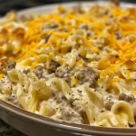 ['A close-up side view of Sour Cream Beef Noodle Casserole, showcasing layers of beef, noodles, and cheese.', 'Juicy Sour Cream Beef Noodle Casserole in a baking dish, highlighting its creamy texture and melted cheese.', 'Side angle photo of a hearty Sour Cream Beef Noodle Casserole, with visible chunks of ground beef and egg noodles.', 'Close-up image of Sour Cream Beef Noodle Casserole, featuring a golden cheesy top and rich beef filling.']